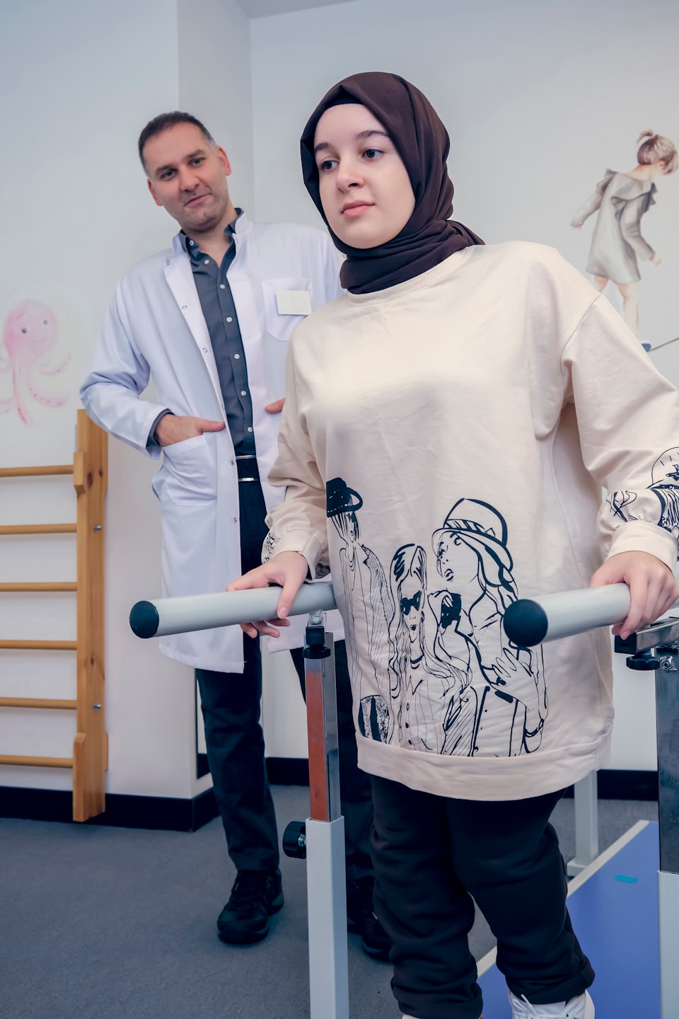 Frau macht Übungen an Barren, während Physiotherapeut zusieht.